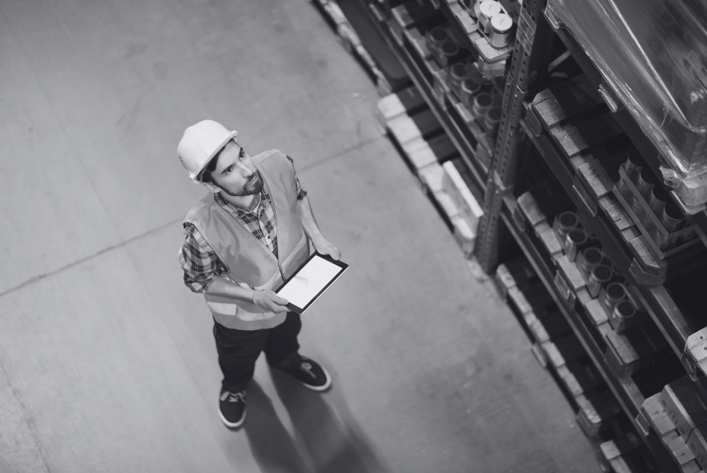 Warehouse worker employed by staffing service checking inventory on tablet.