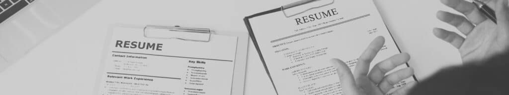 Person holding hands over set of two resumes on table as part of resume screening
